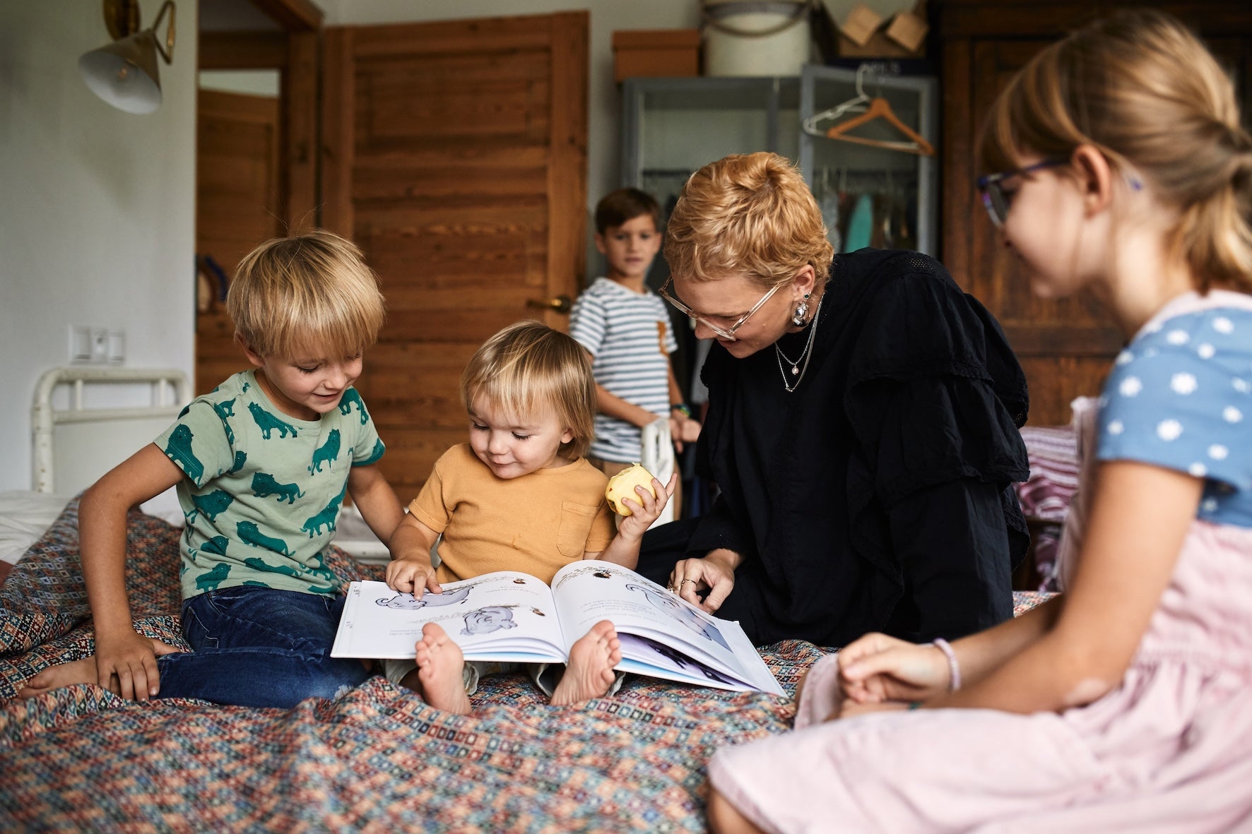 Ein Erwachsener und vier Kinder sitzen lächelnd auf einem Bett und lesen Das Kennlern-Paket vom Zuckersüß Verlag. Umgeben von gemütlichen Holzmöbeln und gedämpfter Beleuchtung teilen sie mit jeder Seite Körperfreundlichkeit und Wärme.
