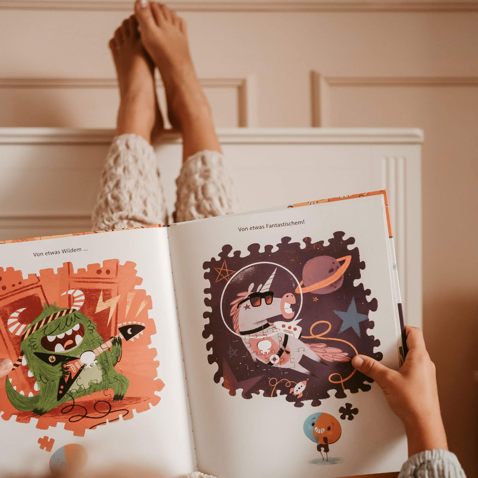 Ein Kind mit hochgelegten Beinen auf einem weißen Heizkörper liest "Einzigartig" von Cale Atkinson, ein farbenfrohes Bilderbuch mit Cartoon-Monstern und skurrilen Illustrationen.