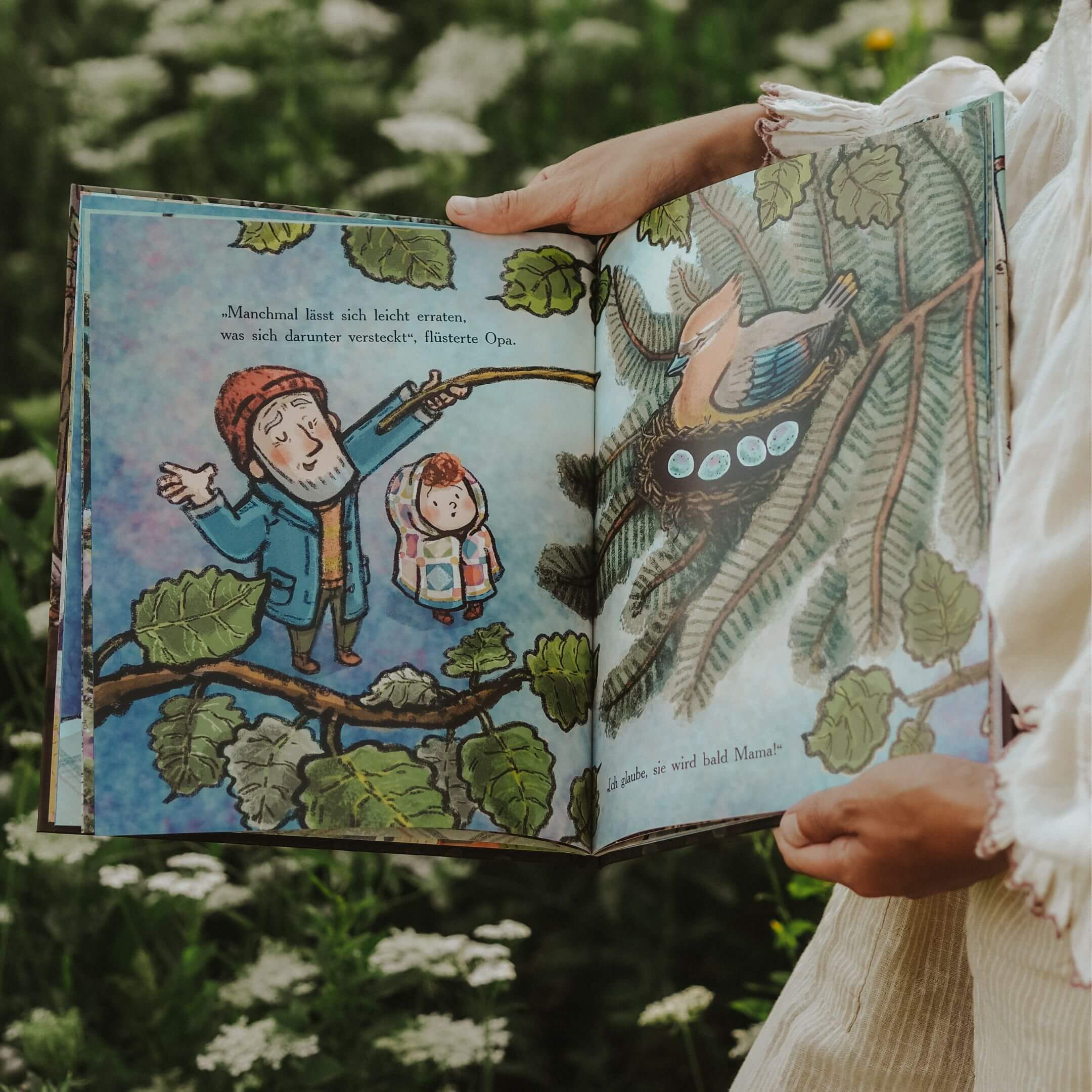 Eine Person hält draußen das aufgeschlagene Bilderbuch "Verborgen" aus dem "Best of Cori Doerrfeld" Paket vom Zuckersüß Verlag in den Händen. Zu sehen sind ein liebevoll illustrierter Großvater und ein Kind, die auf einen Vogel im Nest mit Eiern in den Ästen eines Baumes blicken. Im Hintergrund verschwimmen grüne Blätter und weiße Blumen in natürlicher Umgebung.