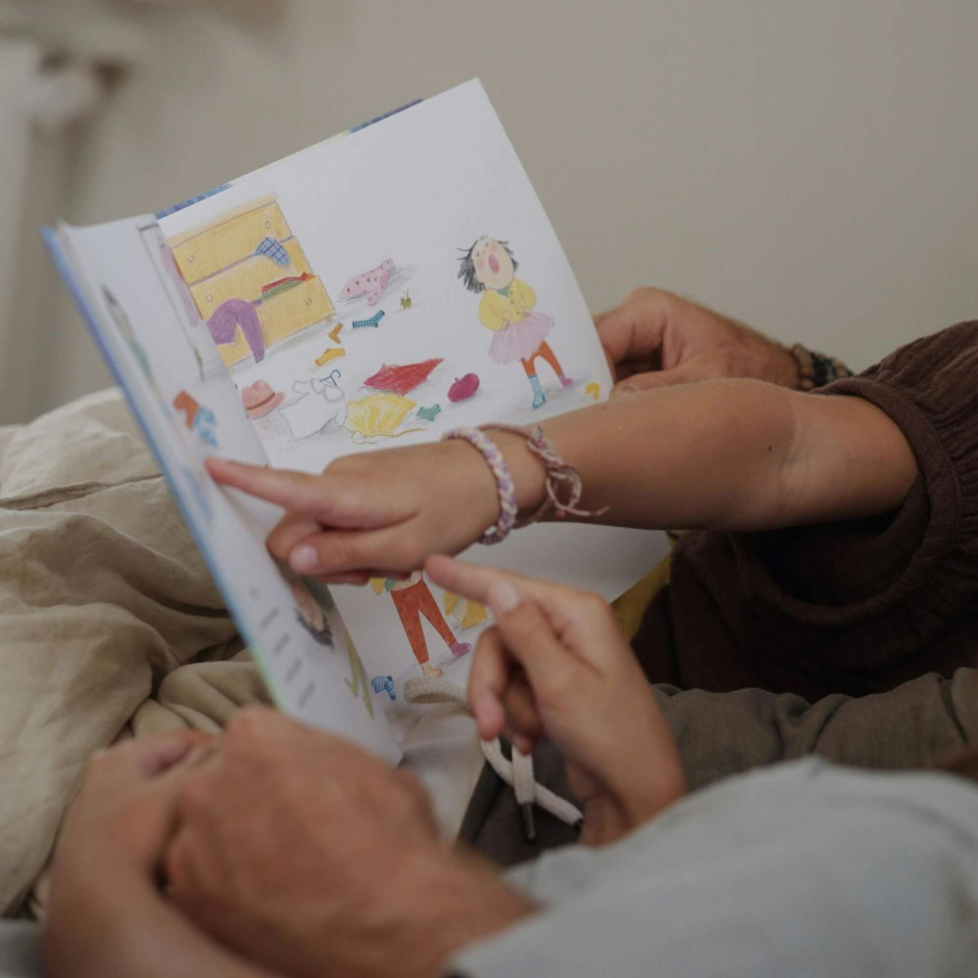 Ein Erwachsener und ein Kind liegen zusammen und lesen "So ein mieser Tag" von Chelsea Lin Wallace. Das Kind zeigt auf eine Illustration, während sich beide mit den bunten Seiten des Buches beschäftigen.