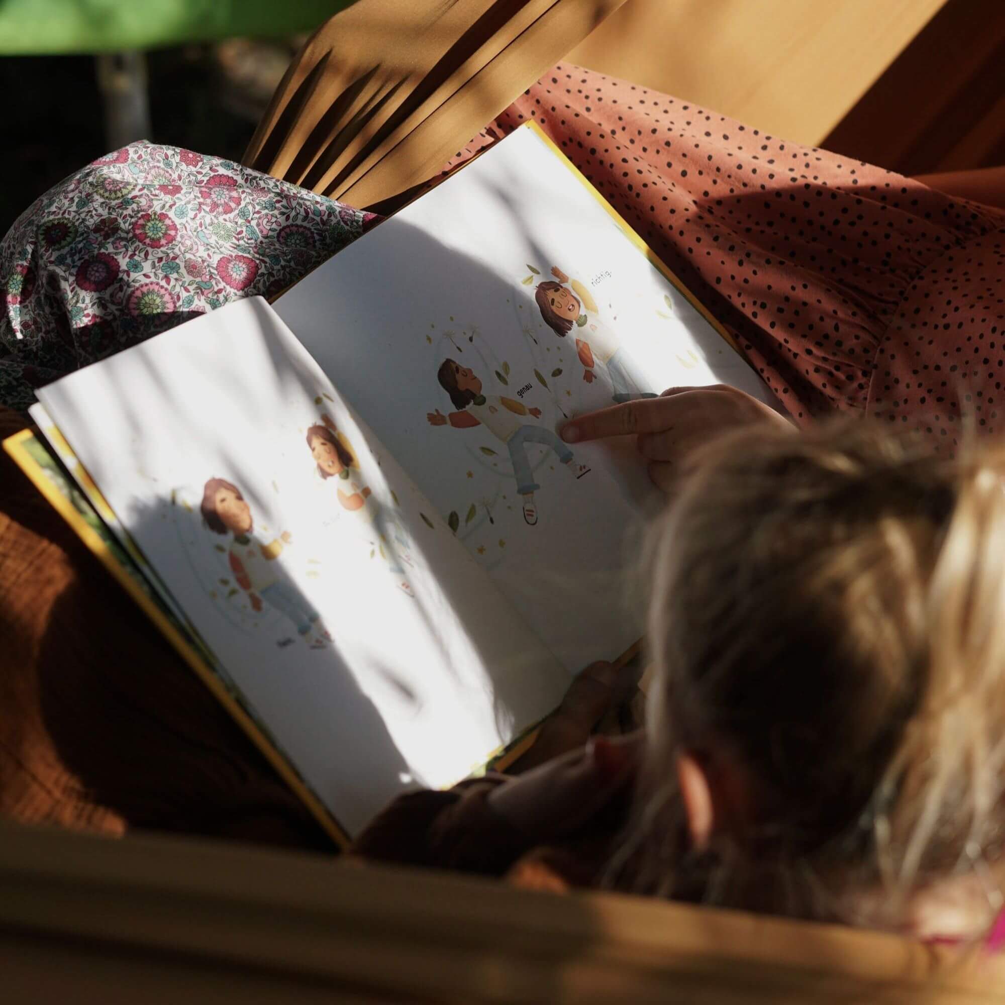 Ein blondes Kind sitzt in einer Hängematte und zeigt auf die Seiten von "Ich bin genau richtig" von Jessica Sanders, während gesprenkeltes Sonnenlicht Schatten auf das Buch und seinen Schoß wirft.
