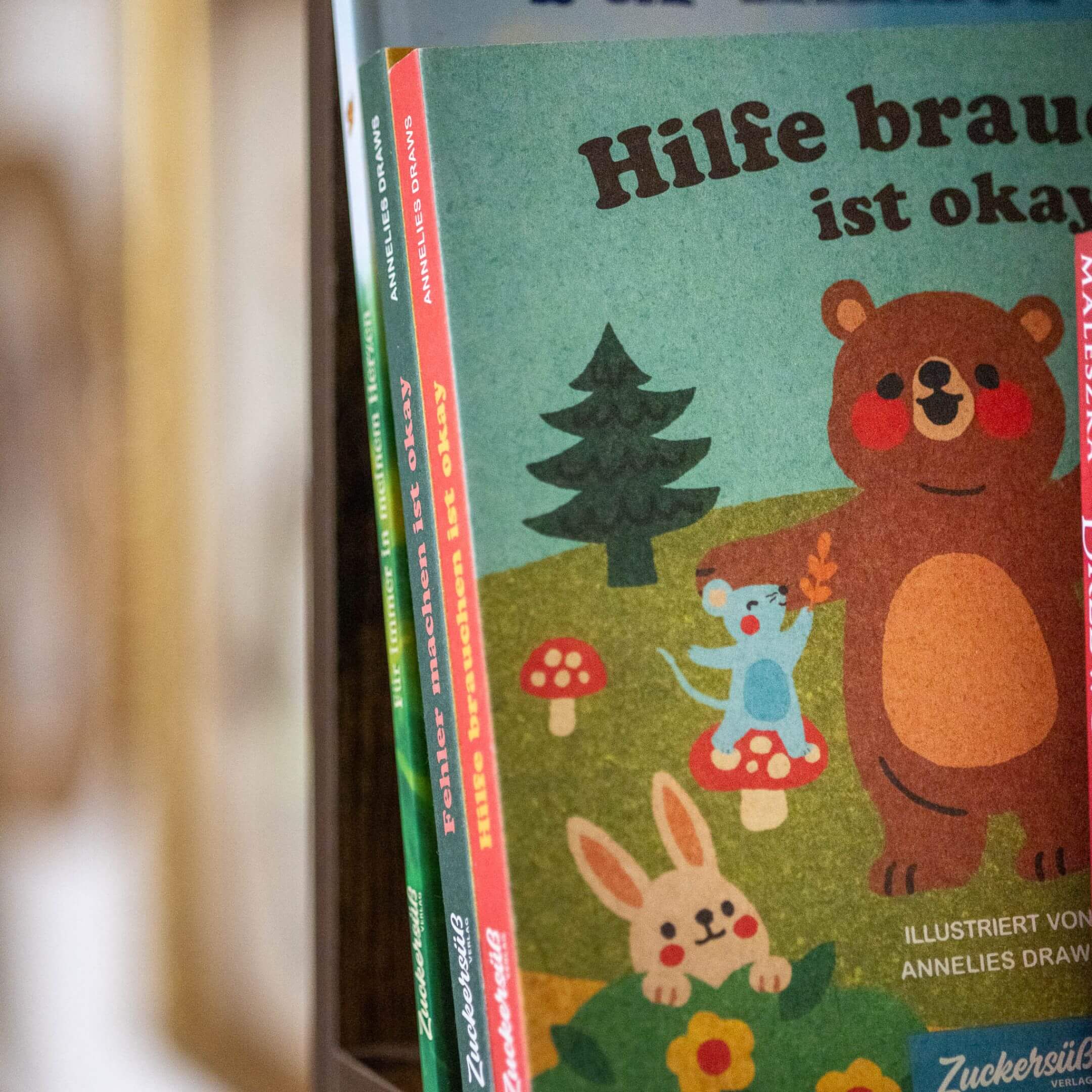 Eine Nahaufnahme von "Hilfe brauchen ist ok" von Annelies Draws, einem farbenfrohen Kinderbuch mit einem lächelnden Bären, einer blauen Maus, einem Hasen und roten Pilzen auf dem Cover.