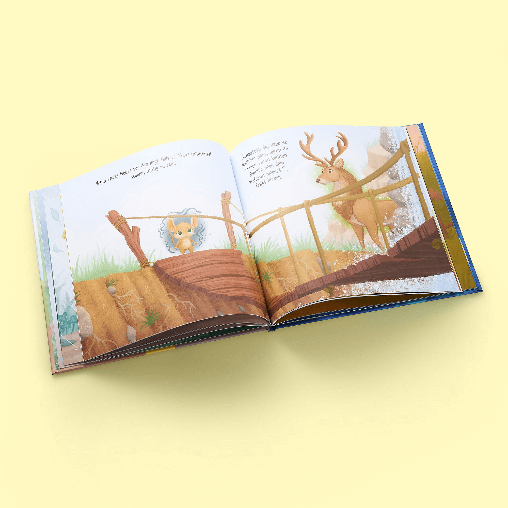 Ein aufgeschlagenes Exemplar von "Immer weiter" aus dem Zuckersüß Verlag liegt auf einem gelben Hintergrund und zeigt auf der linken Seite eine Maus auf einer Holzbrücke und auf der rechten Seite einen Hirsch auf der Brücke, beide in einer grasbewachsenen Landschaft.
