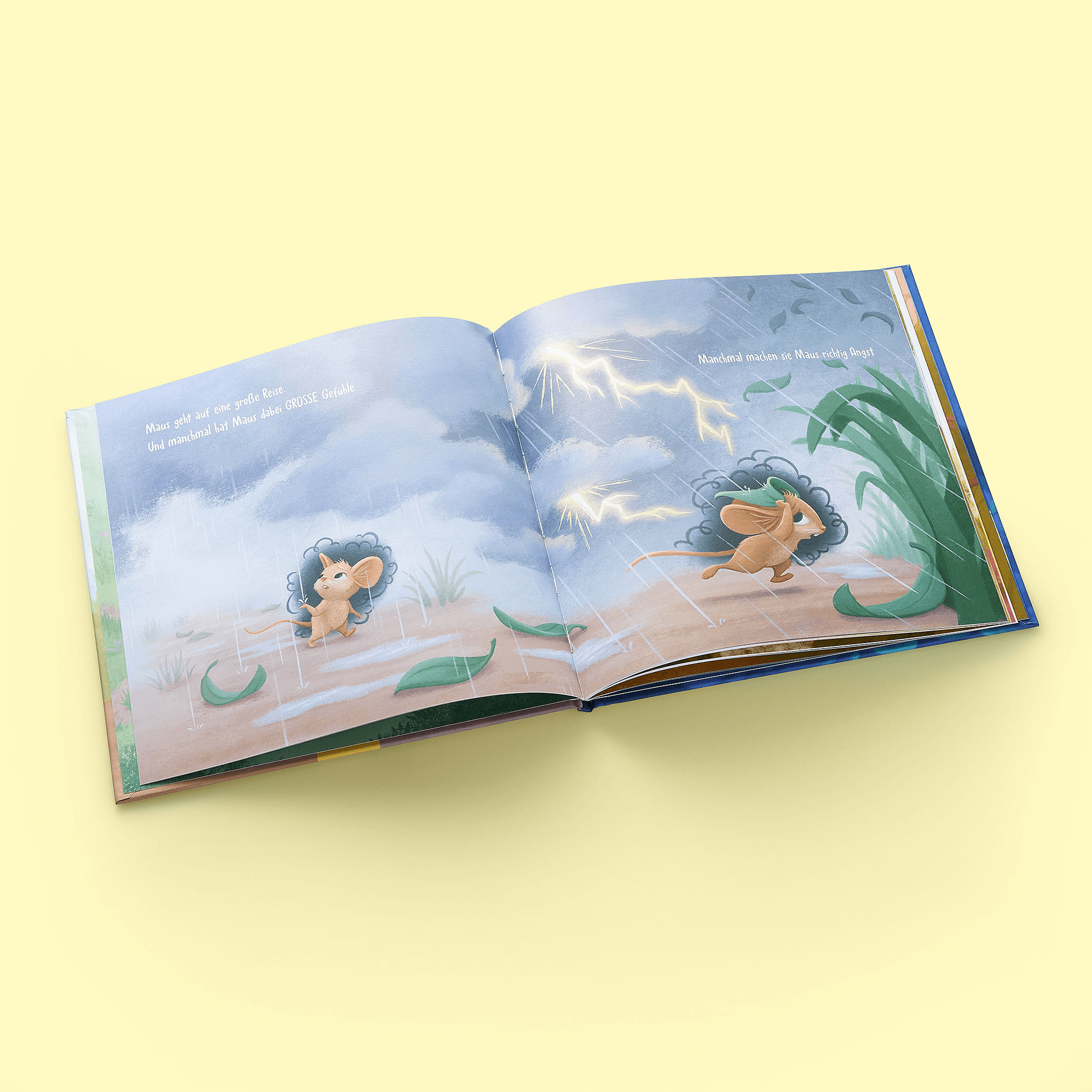 Ein aufgeschlagenes Exemplar von "Immer weiter" aus dem Zuckersüß Verlag zeigt zwei junge Löwen, die zwischen grünen Pflanzen auf hellgelbem Hintergrund in einen blitzenden Himmel blicken und Kindern helfen, ihre Gefühle zu erkennen und zu verarbeiten.