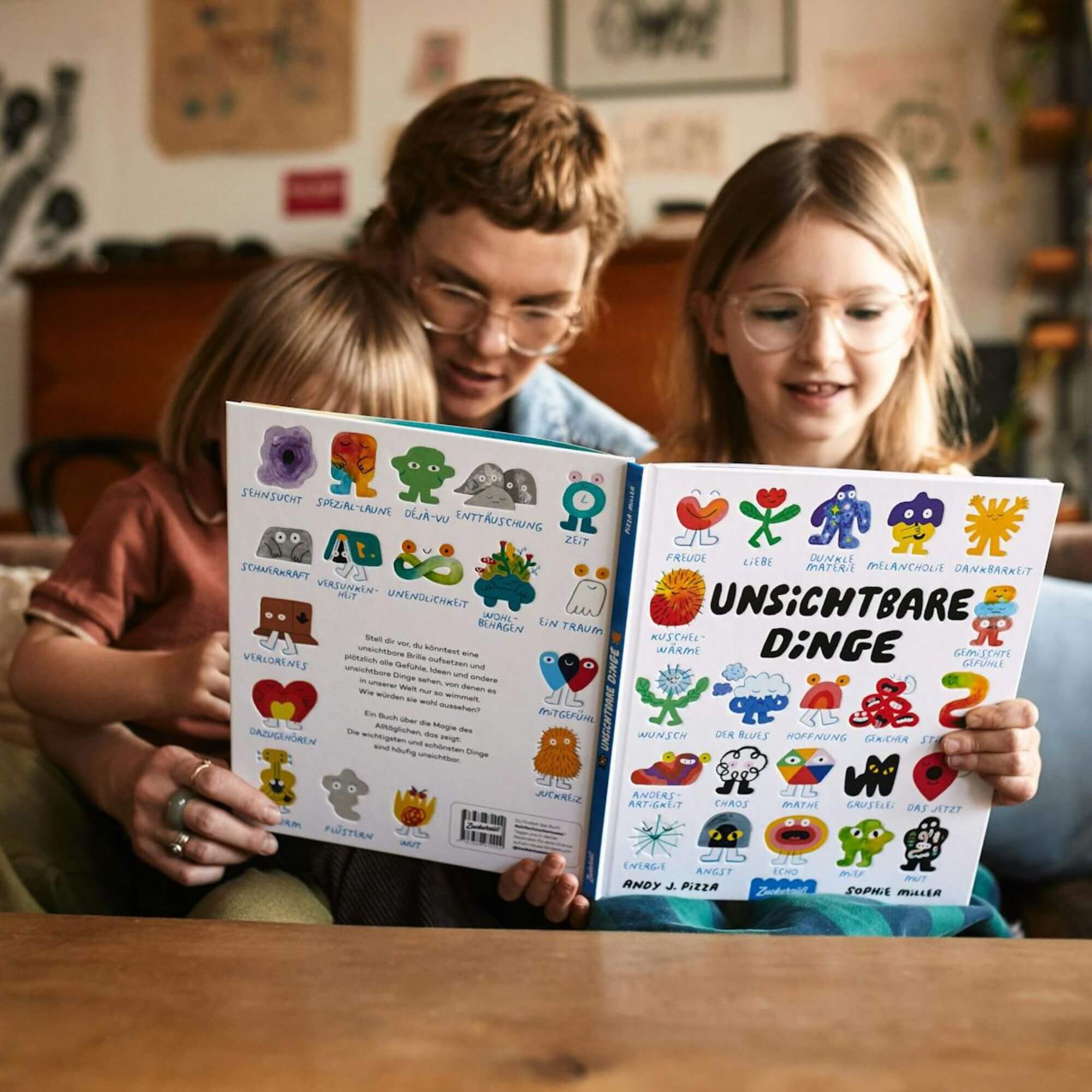Eine erwachsene Person und zwei Kinder sitzen gemeinsam auf einem gemütlichen Sofa und lächeln beim Lesen des farbenfrohen Bilderbuchs „Unsichtbare Dinge“ von Andy J. Pizza und Sophie Miller. Umgeben von verspielten gezeichneter Figuren.