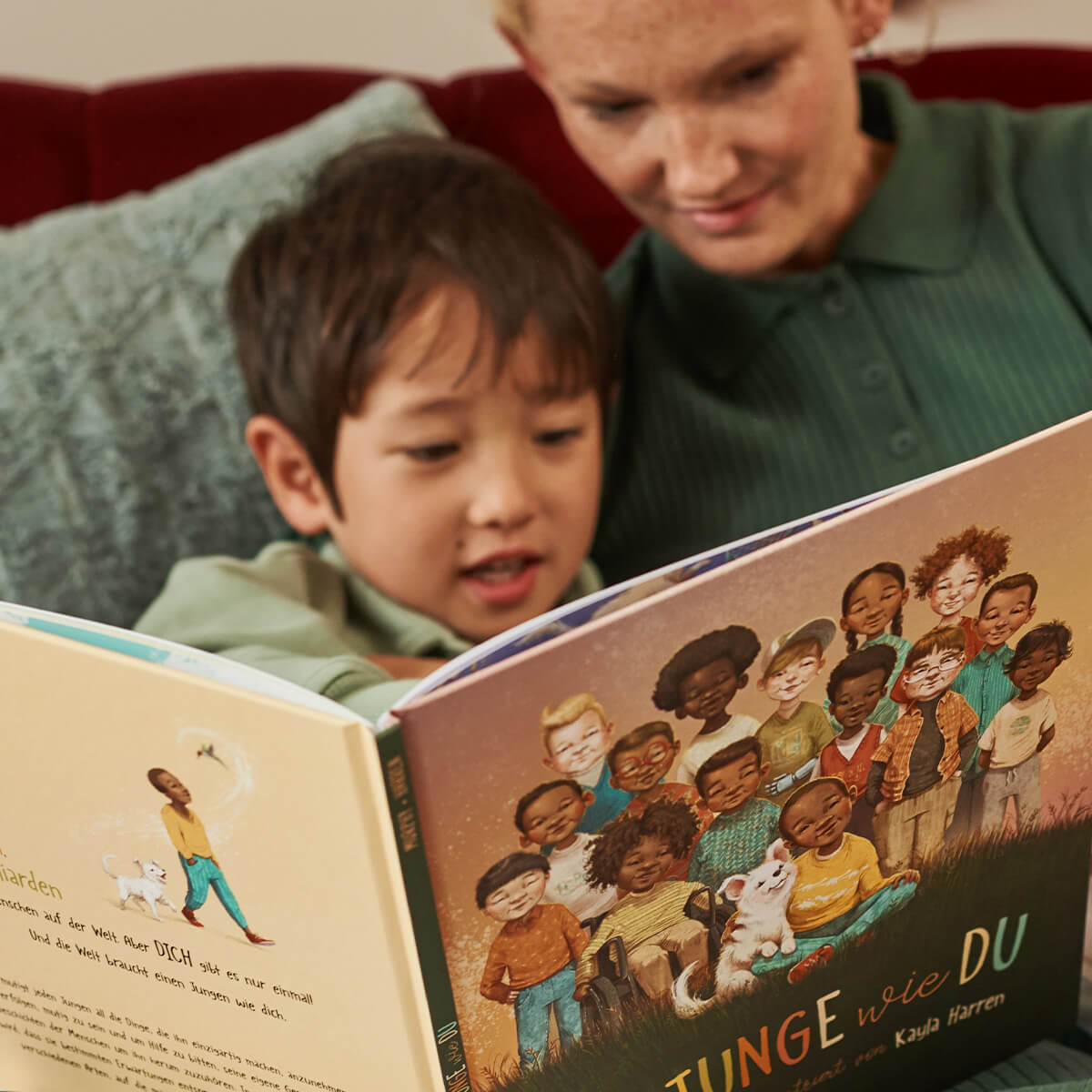 Eine erwachsene Person und ein kleines Kind sitzen auf einer Couch und lesen "Ein Junge wie du" von Frank Murphy, ein Kinderbuch mit bunten Illustrationen verschiedener Kinder und einem weißen Hund auf dem Cover.