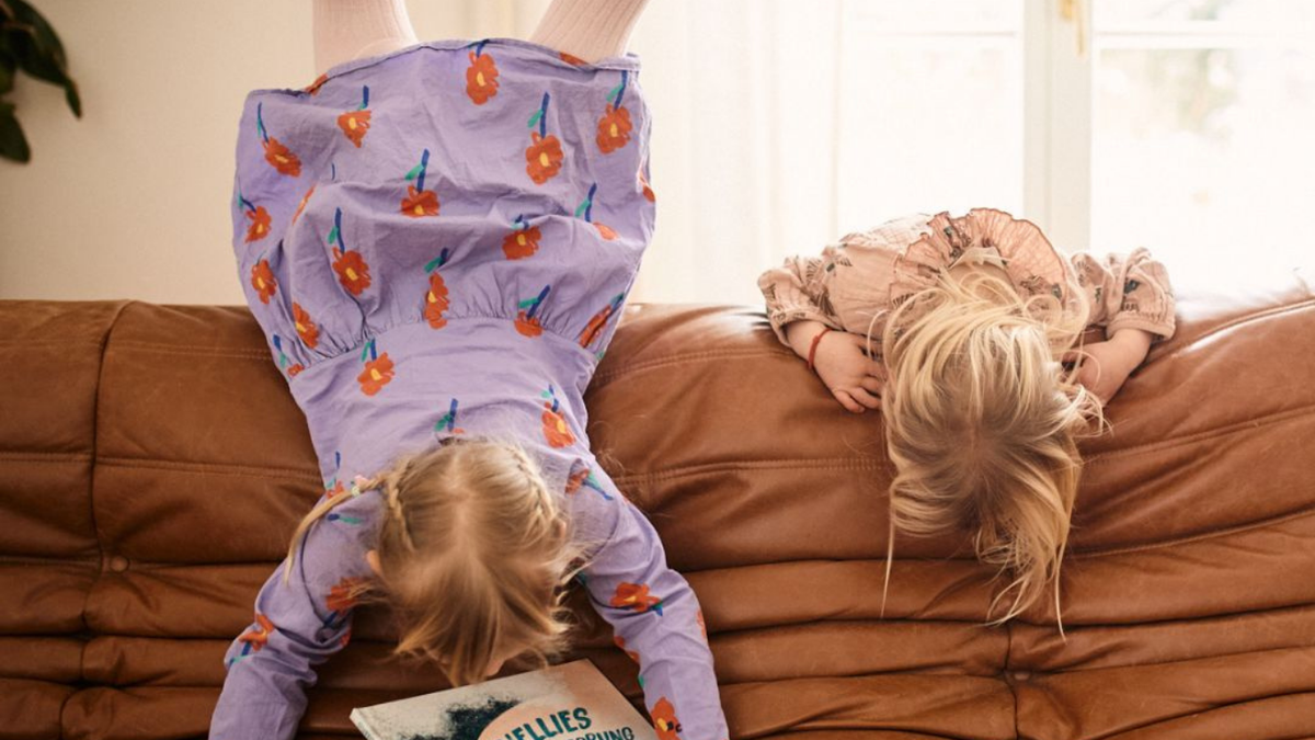Zwei Kindern hängen kopfüber auf einem Sofa. 