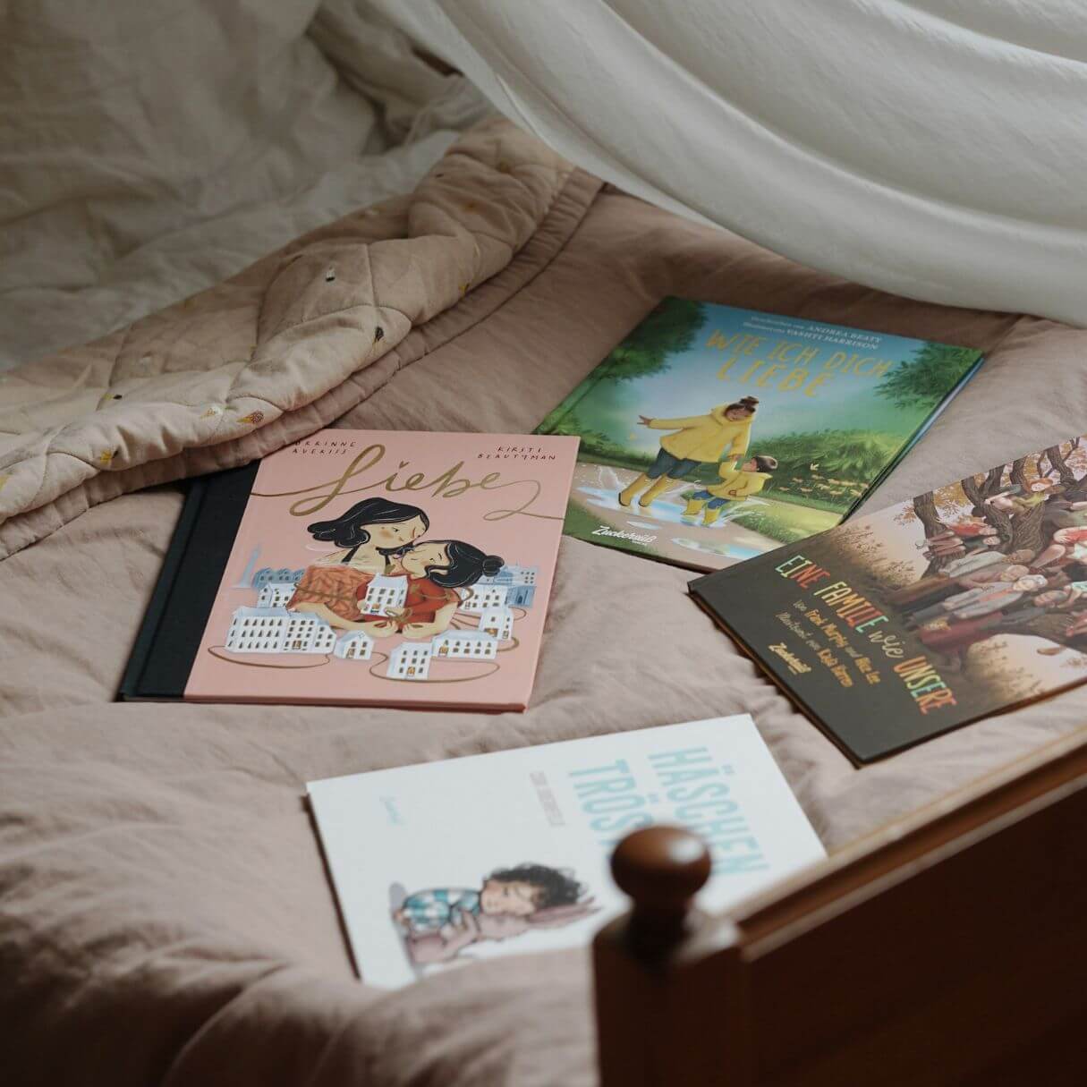 Vier illustrierte Kinderbücher liegen auf einem ordentlich gemachten Bett mit einer beigen Bettdecke und einem Holzrahmen unter sanftem Tageslicht.