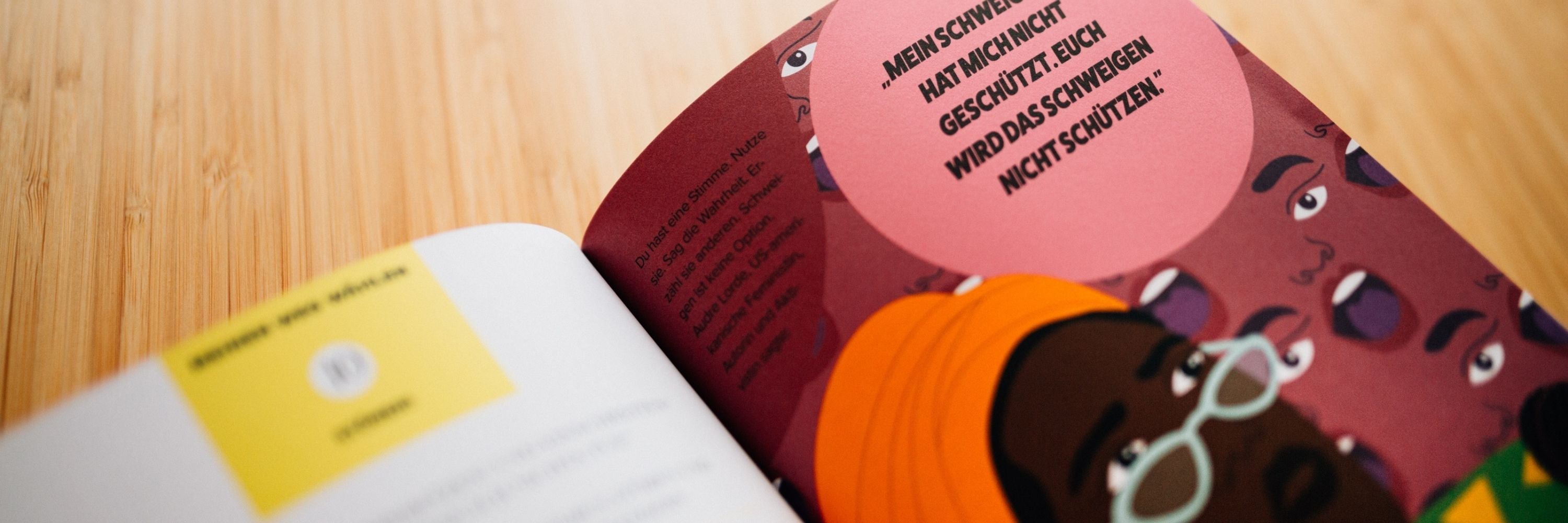 Ein aufgeschlagenes Buch auf einer hölzernen Oberfläche, das bunte Illustrationen von Gesichtern und deutschen Text in einer Sprechblase auf der rechten Seite zeigt. Die linke Seite enthält einen gelben Abschnitt mit Text.