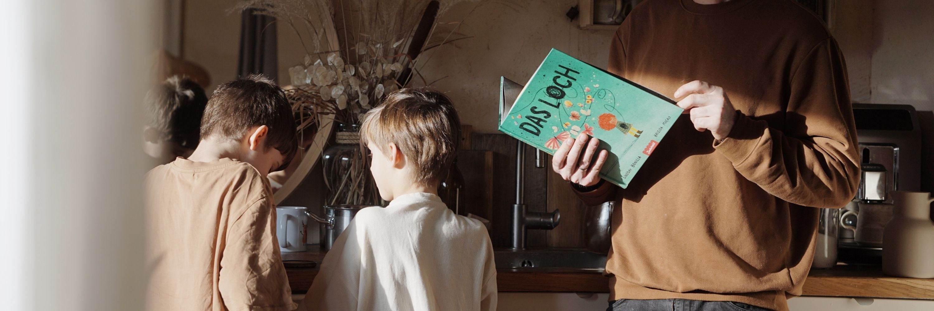 Ein Erwachsener liest neben zwei Kindern "Das Loch"