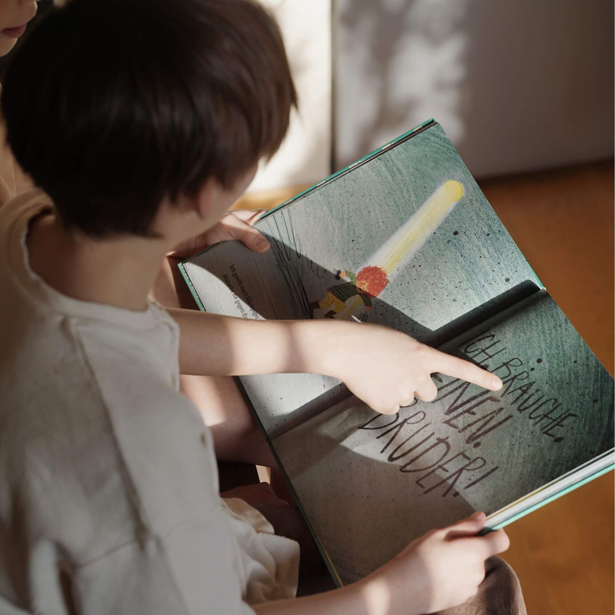 Ein kleines Kind liest "Das Loch" von Lindsay Bonilla und zeigt auf den handgeschriebenen Text, während warmes Licht die Illustration einer Figur mit einem leuchtenden Gegenstand beleuchtet, der an Erinnerung erinnert.