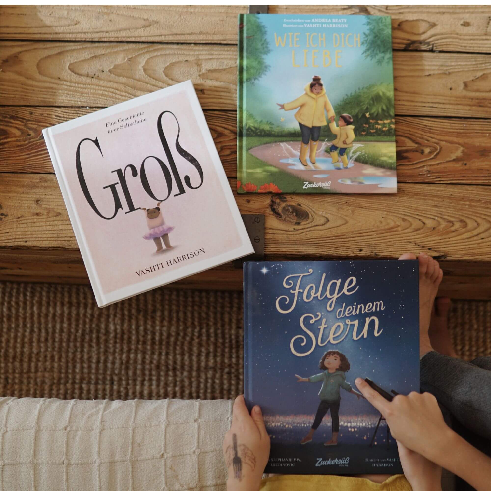 Drei herzerwärmende Bücher der Reihe "Best of Vashti Harrison" von Zuckersüß Verlag liegen auf einem Holztisch.