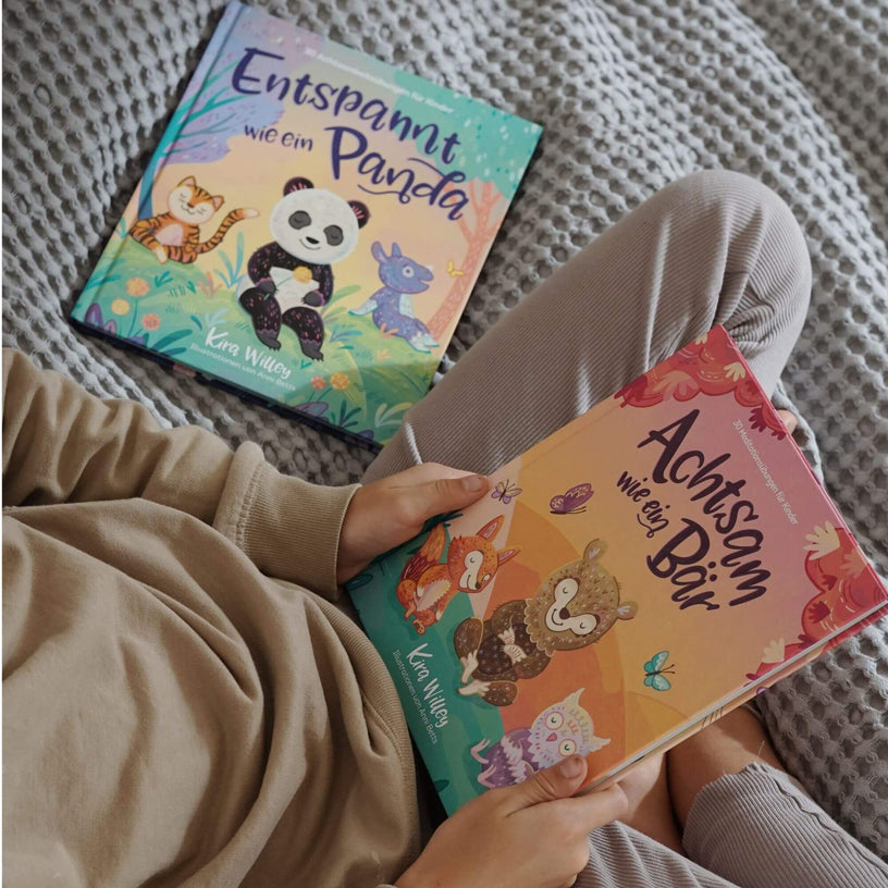 Ein Kind in beigefarbener Kleidung sitzt auf einer grauen Decke und hält das Buch „Achtsam wie ein Bär“ aus dem Doppelset „Achtsamkeit im Doppelpack“ des Zuckersüß Verlags in den Händen. Daneben liegt das zweite Buch der Reihe, „Entspannt wie ein Panda“. Beide Titel zeigen liebevoll illustrierte Tiere.