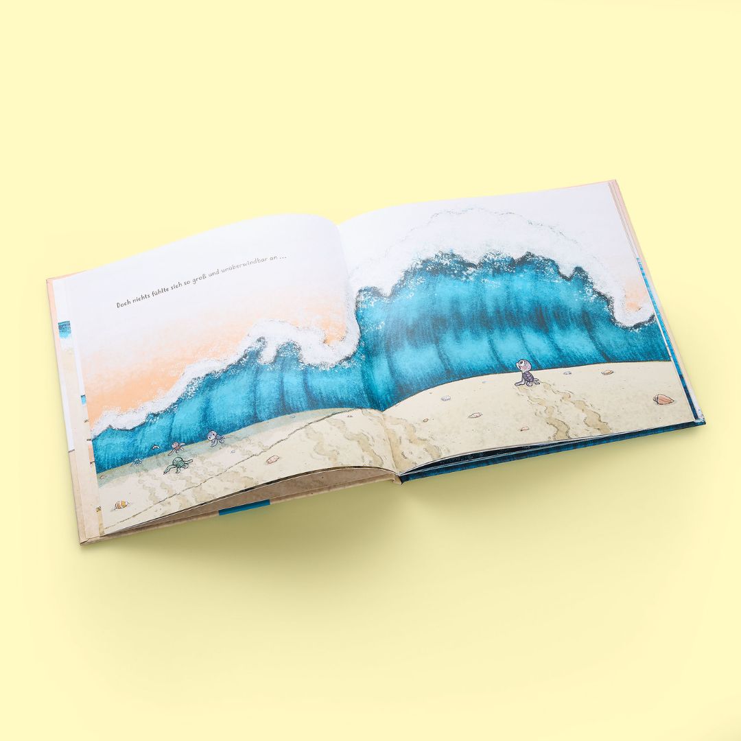 Ein aufgeschlagenes illustriertes Kinderbuch "Nellies großer Sprung" vom Zuckersüß Verlag liegt auf gelbem Hintergrund und zeigt eine große Meereswelle, die auf einen Sandstrand mit kleinen Figuren rollt; der Text in der Ecke erinnert an Mut und innere Stärke.