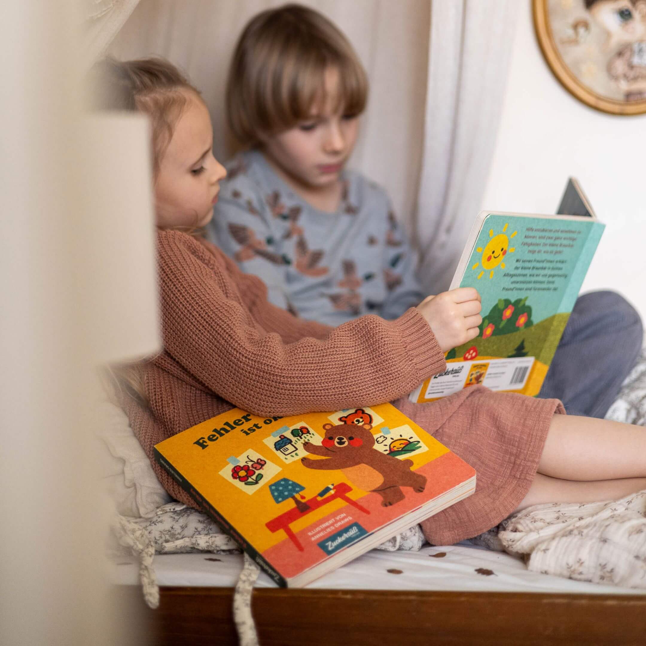Zwei kleine Kinder kuscheln auf einem gemütlichen Bett und lesen bunte Kinderbücher. Das eine hält 