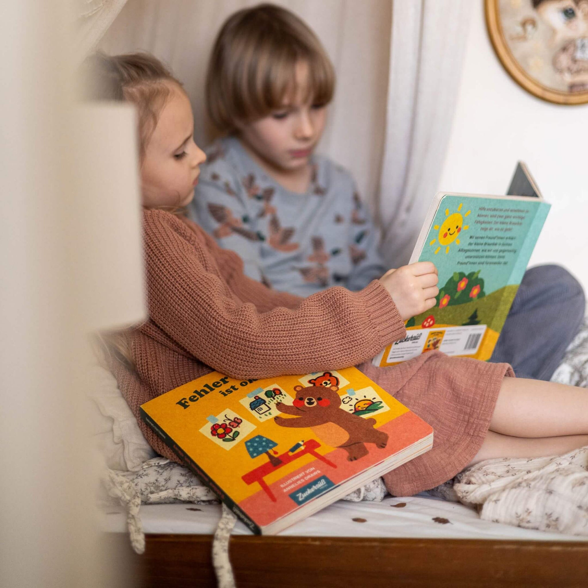 Zwei kleine Kinder kuscheln auf einem gemütlichen Bett und lesen bunte Kinderbücher. Das eine hält 