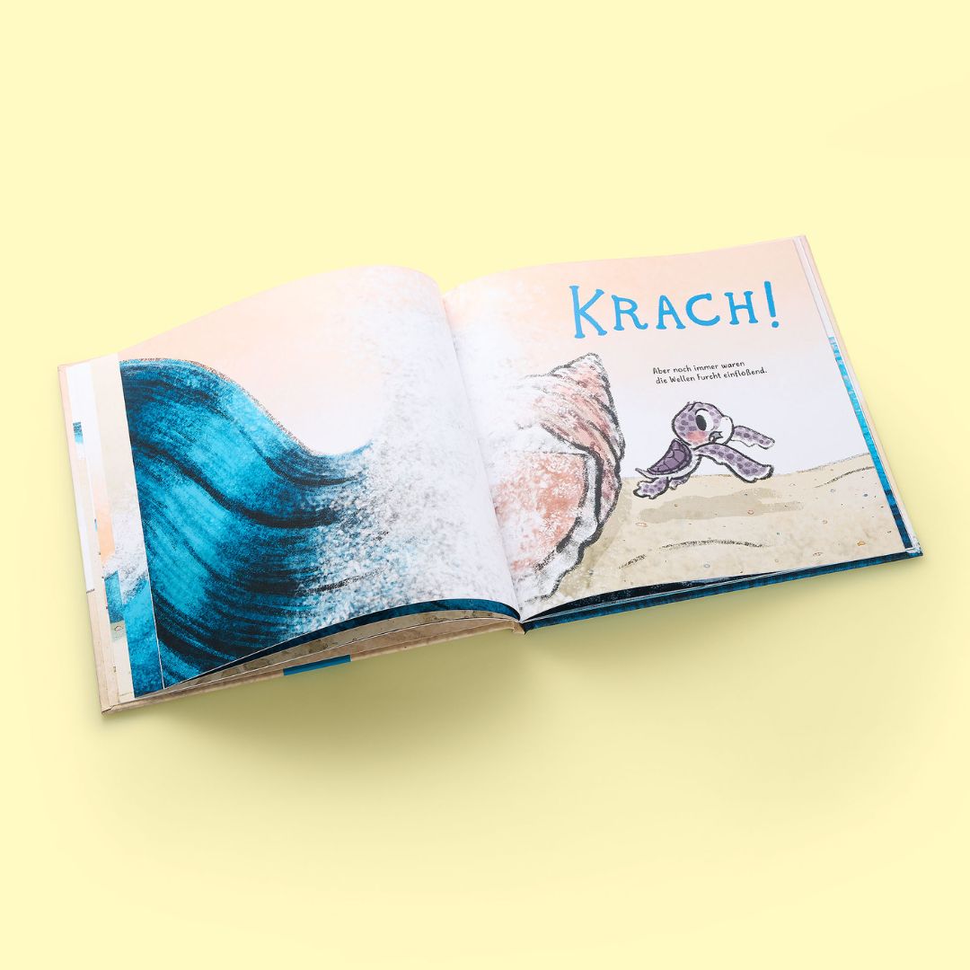 Auf einer hellgelben Fläche liegt ein aufgeschlagenes Exemplar von "Nellies großer Sprung" aus dem Zuckersüß Verlag, das eine blaue Welle, einen lila Oktopus und das Wort "KRACH!" zeigt - eine Szene, die Mut und innere Stärke symbolisiert.