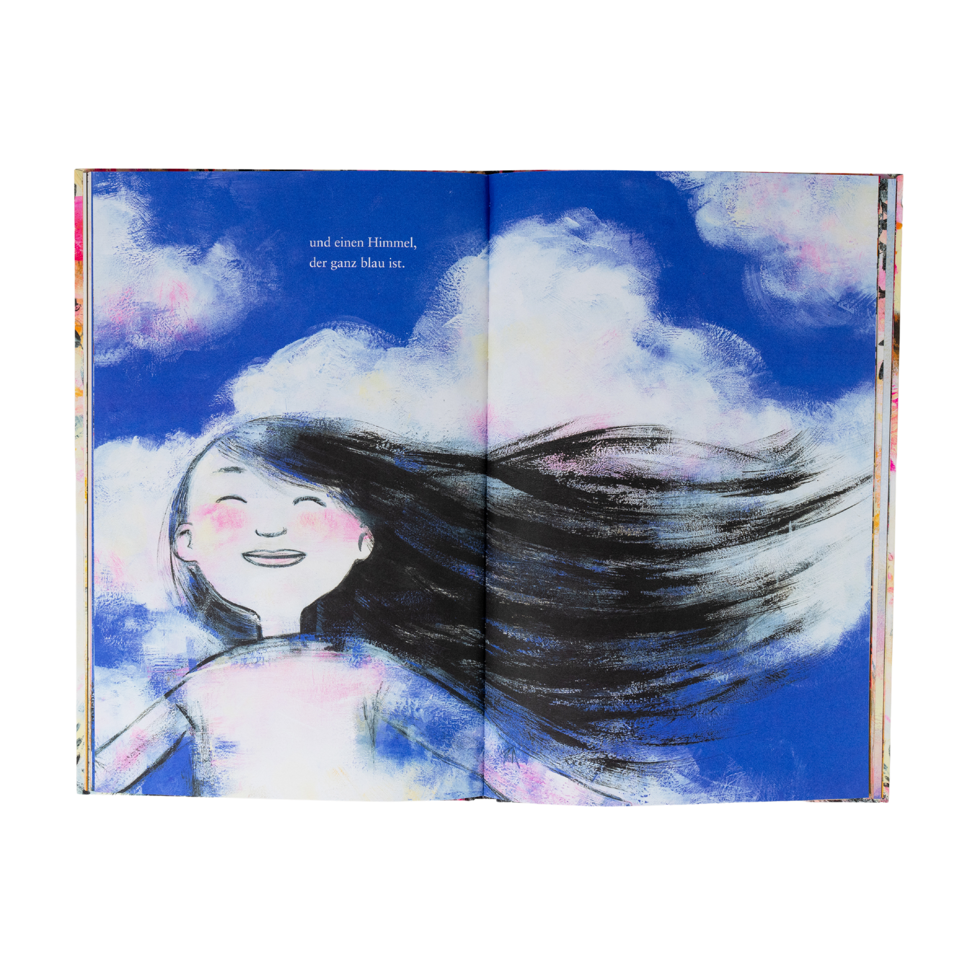 Ein illustriertes Mädchen mit langen schwarzen Haaren lächelt mit geschlossenen Augen vor einem strahlend blauen Himmel mit Schäfchenwolken. Aus "Der Baum in mir" von Corinna Luyken. Deutscher Text links: und ein Himmel, der ganz blau ist.