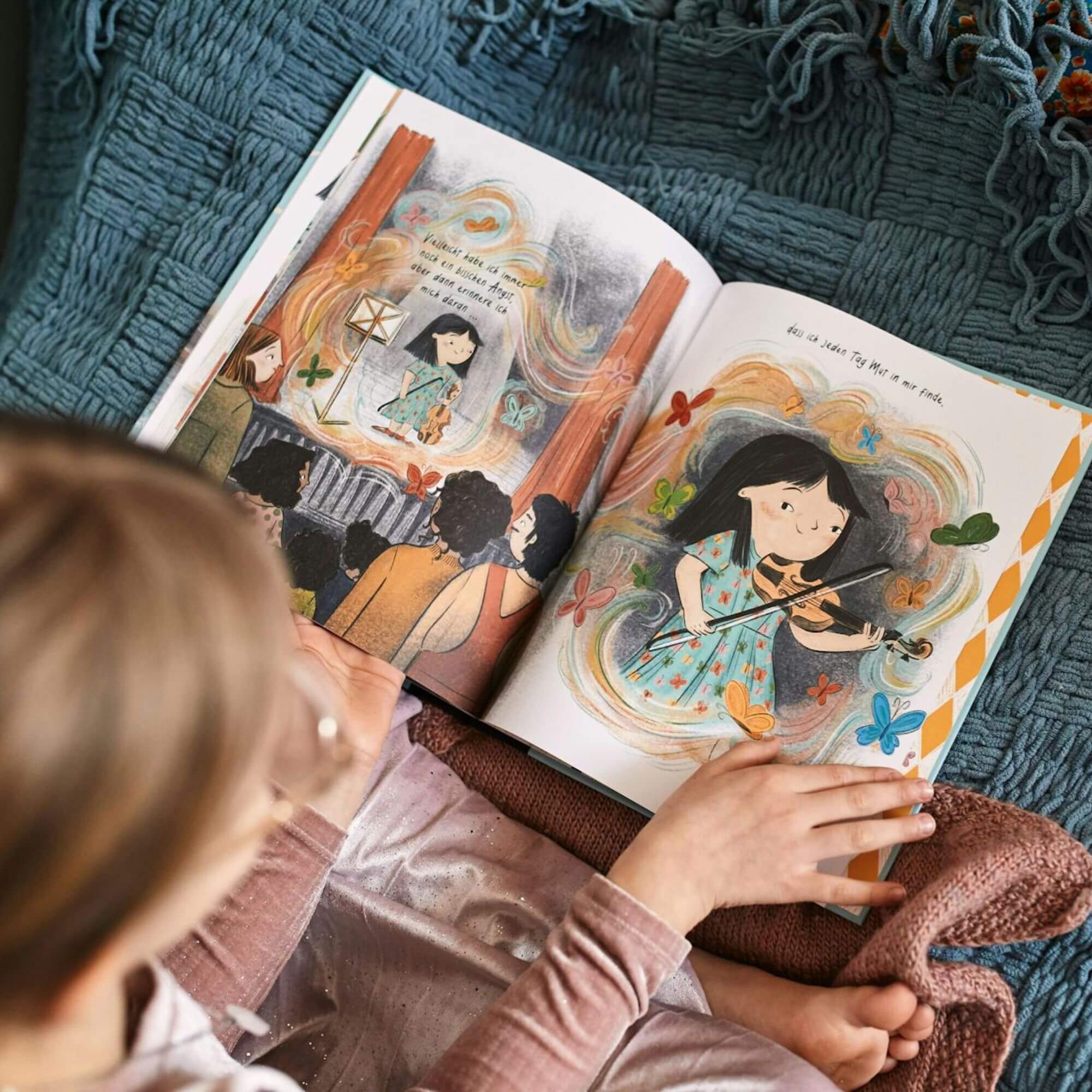 Ein junges Kind sitzt auf einer Decke und liest Mut von Wai Mei Wong – ein farbenfrohes Bilderbuch mit Illustrationen eines Kindes, das von wirbelnden Mustern und Schmetterlingen umgeben ist.