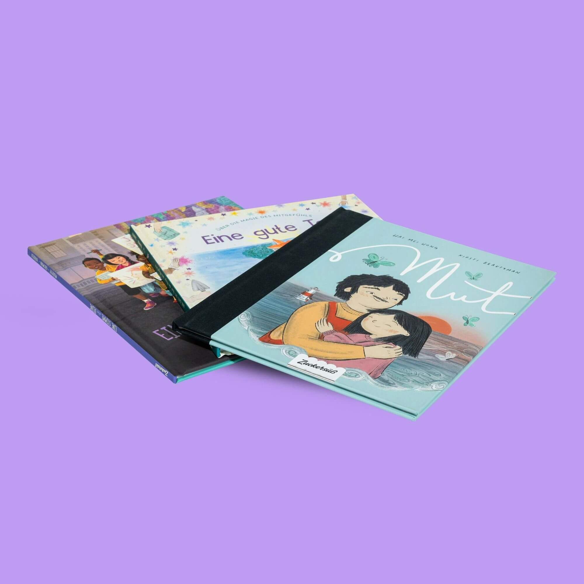 Drei illustrierte Kinderbücher aus dem "Das Optimismus-Paket" des Zuckersüß Verlags sind auf einem lila Hintergrund gestapelt. Das oberste Buch, "Mut", zeigt ein Kind, das einen Erwachsenen umarmt.