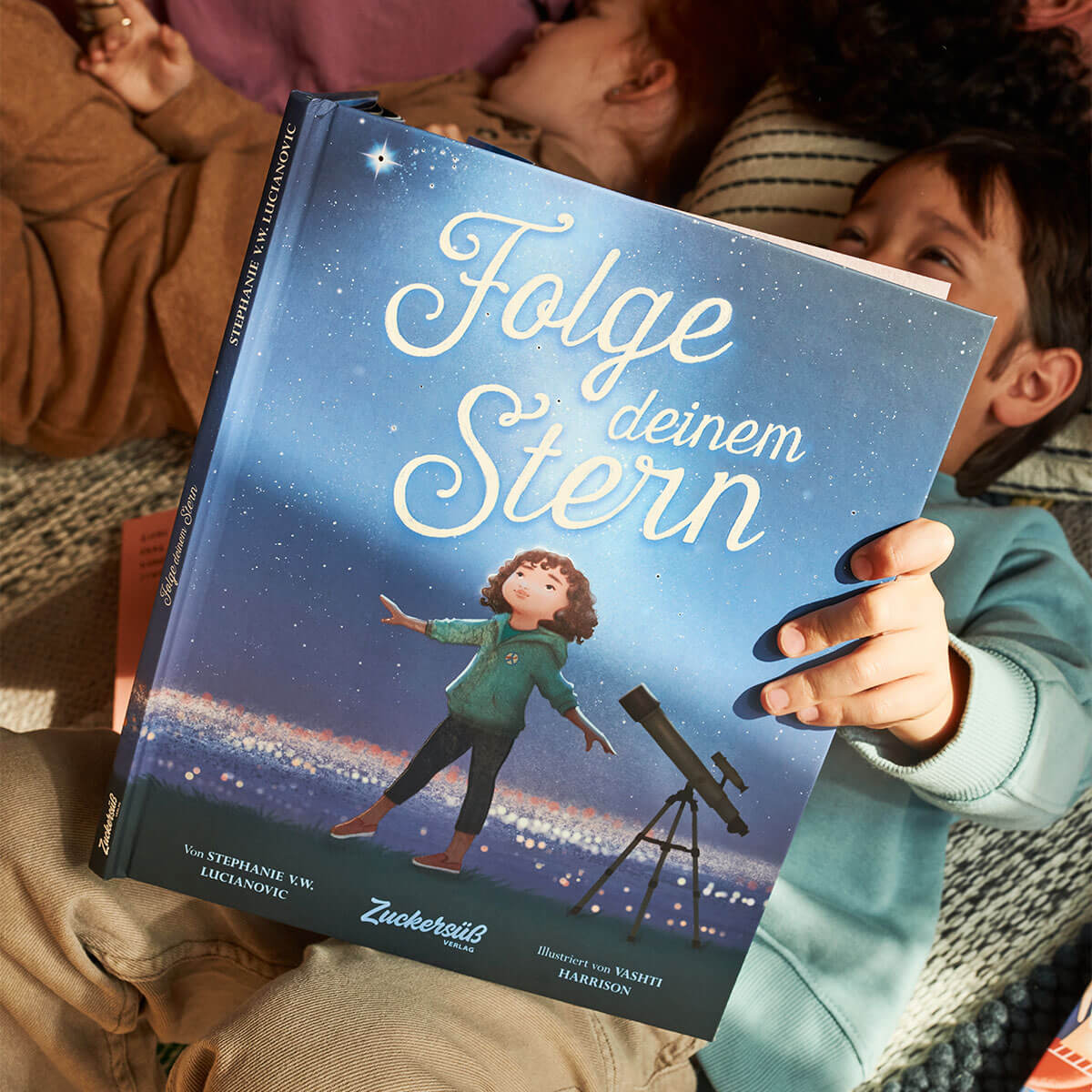 Ein Kind hält "Folge deinem Stern" von Stephanie V.W. Lucianovic in der Hand. Das Titelbild zeigt ein Kind mit einem Teleskop unter dem Sternenhimmel, während ein anderes Kind im Hintergrund lächelt und das Wunder des Weltraums und der Träume festhält.